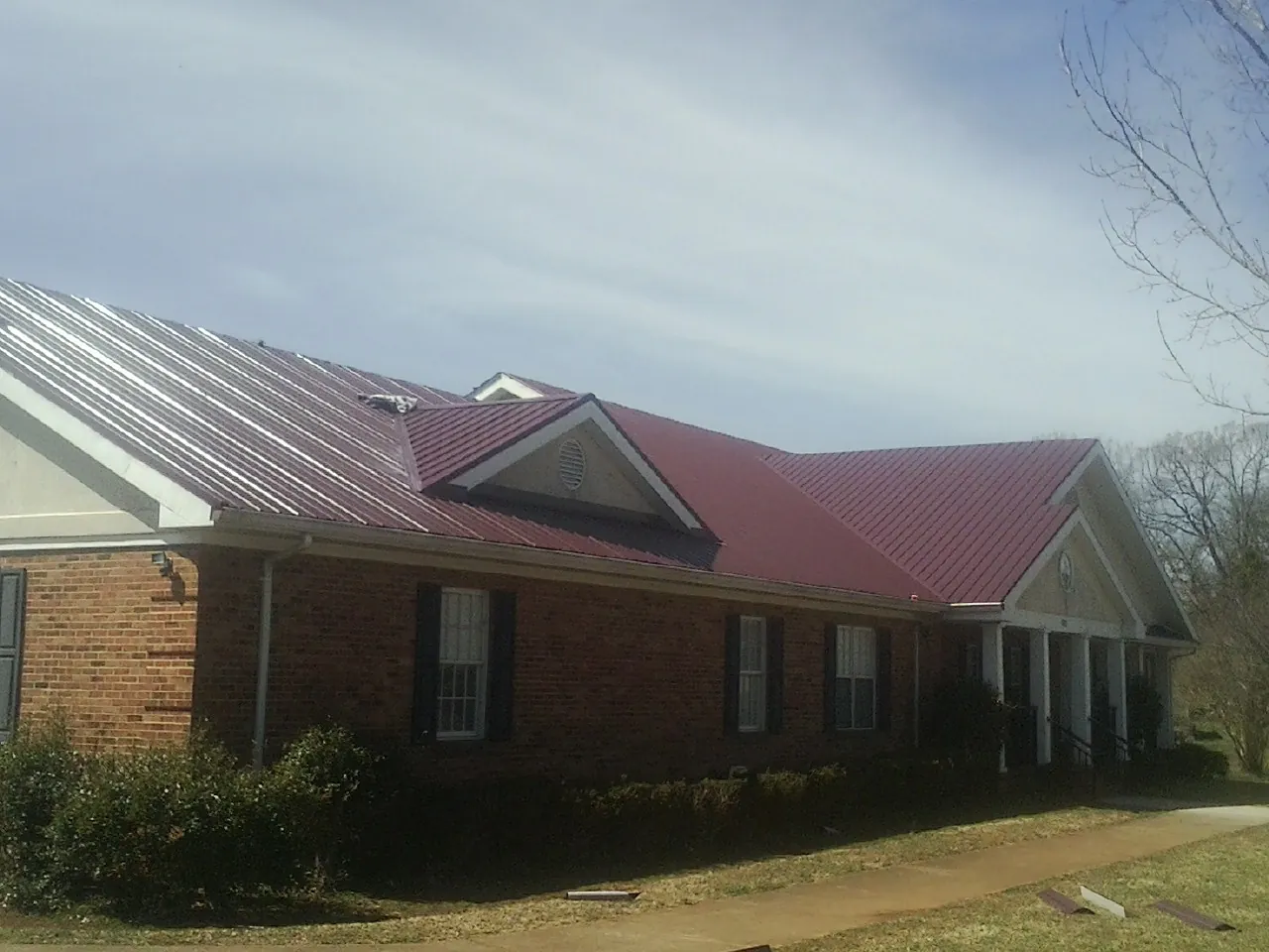 Red metal roof with gabled entries on a long brick building, from a Hail Damage Roof Repair job in Newbern