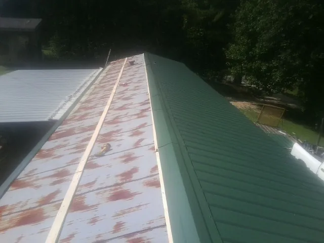 Old rusted panels beside newly installed green metal roofing — Wind Damage Roof Repair by Roofing Brothers in Newbern
