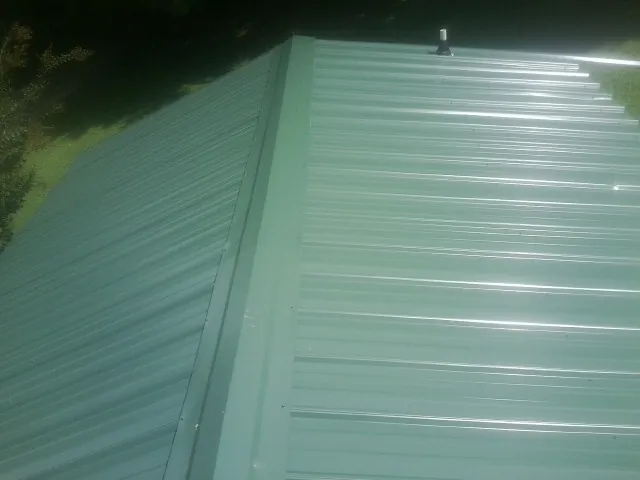 New green metal panels meeting at the ridge of a roof — Flat Roof Repair work by our crew in Newbern