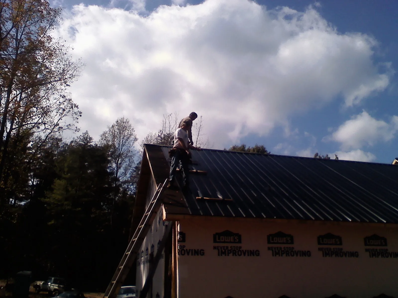 Roofer fastening dark metal panels high against a cloudy sky, from a Roof Inspection job in Newbern