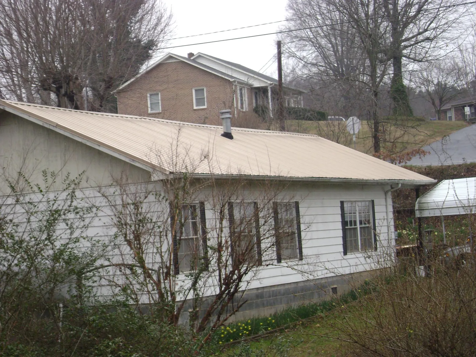 Tan metal roof on a white sided house set into a hillside — Commercial Roofing by Roofing Brothers in Newbern